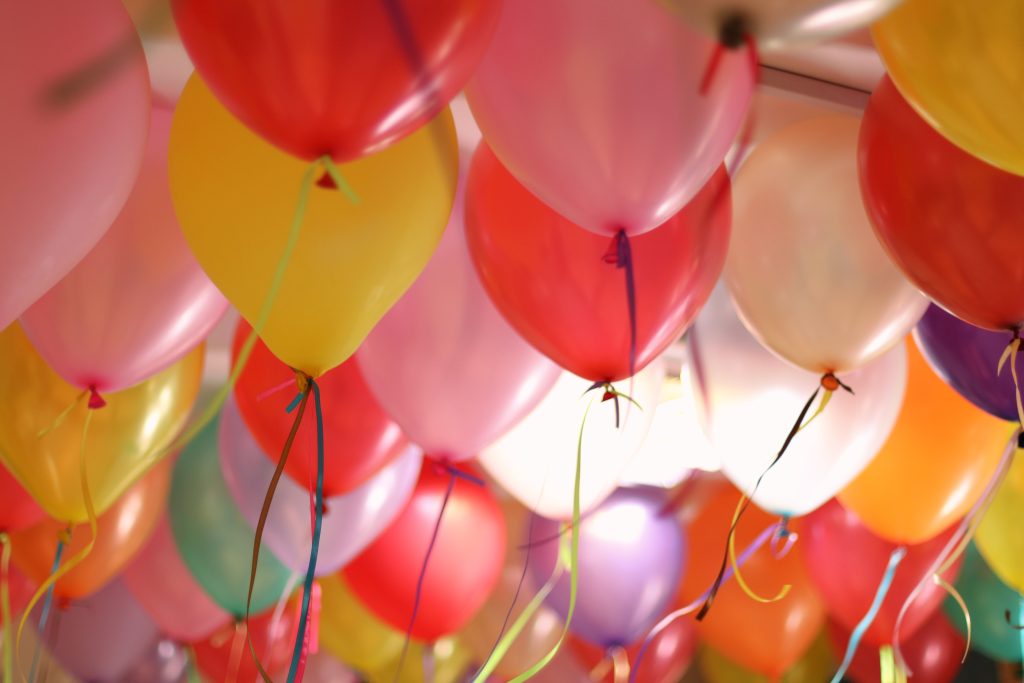 Balloons (in pink, yellow, purple and green) collect on the ceiling of a room