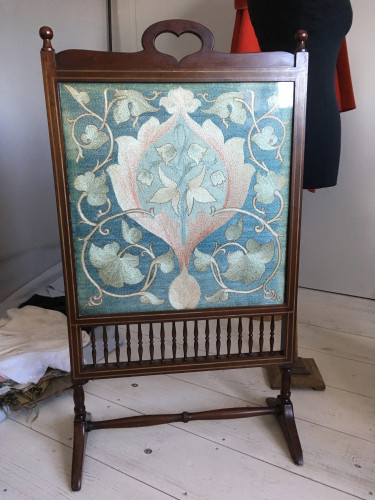 wooden firescreen with heart shape at top holding embroidery of pink leaves against blue ground