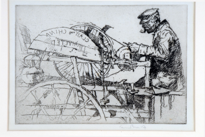 Man in peaked cap with pipe seated at knife grinder's wheel