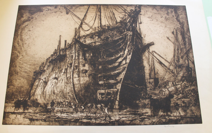 Image of a large ship moored in dockyard, demolition crews in foreground and around ship, cranes and hoists in distance beyond