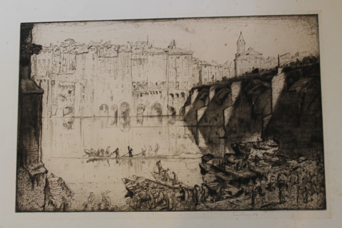 Figures on quayside with boats moored on river foreground, figures in boats hauling in nets on river beyond, bridge with figures crossing right, with view across river to houses and churches background
