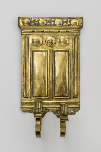 A brass candle sconce for holding two candles, it features stars and faces
