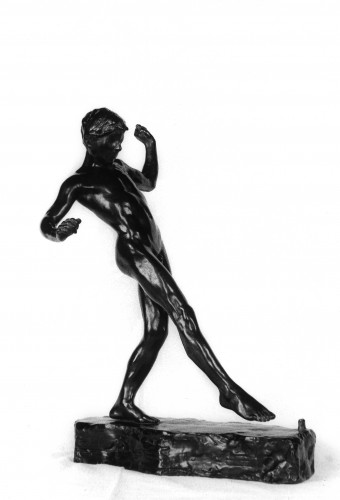 Boy standing balancing himself on one foot, reaching forward with other foot to touch a knucklebone on ground in front of him