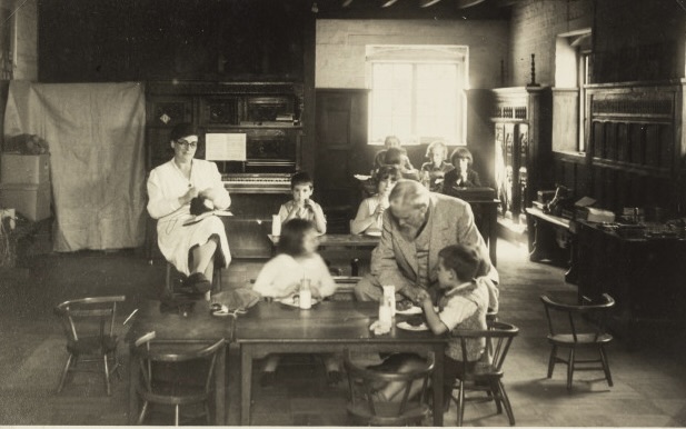 An elderly Frank Brangwyn sits at a table with evacuee children