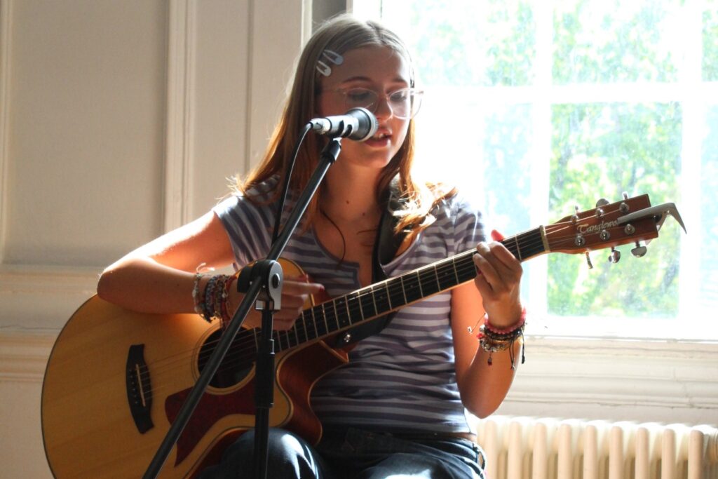 Performer sits to play guitar and sing