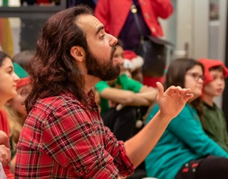 A man in profile who is speaking to an audience. His hand is raised as he tells a story.